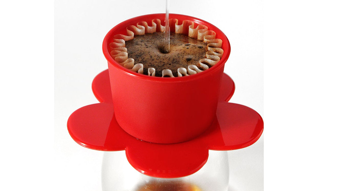 Red coffee filter with coffee being dripped into a glass container on a white background