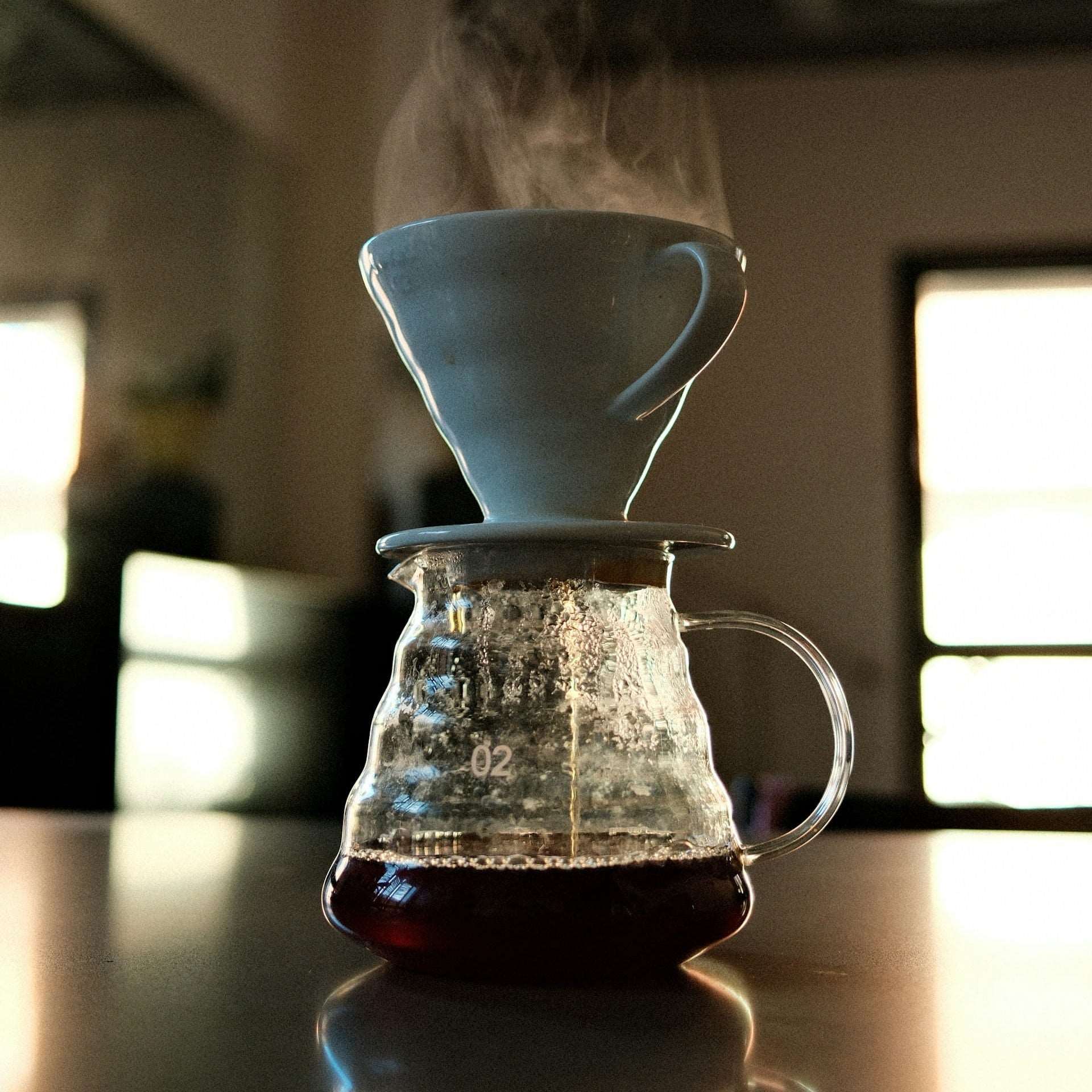 Coffee brewing process with a glass carafe and white mug on a reflective surface.