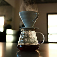Coffee brewing process with a glass carafe and white mug on a reflective surface.